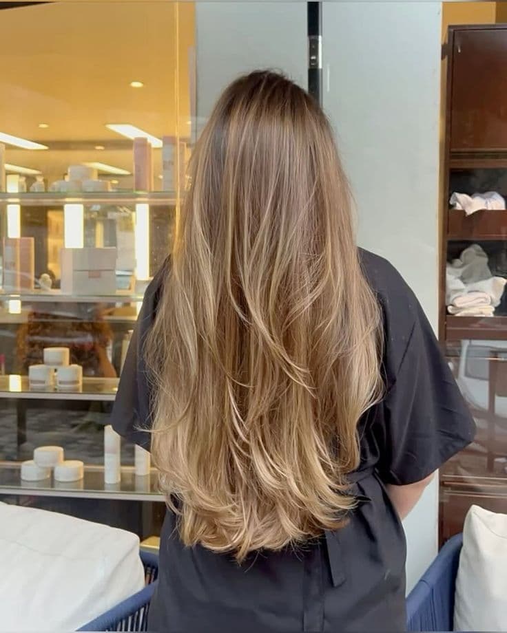 Vista de costas de cabelo longo castanho-claro, cortado em camadas repicadas e com mechas iluminadas nas pontas.