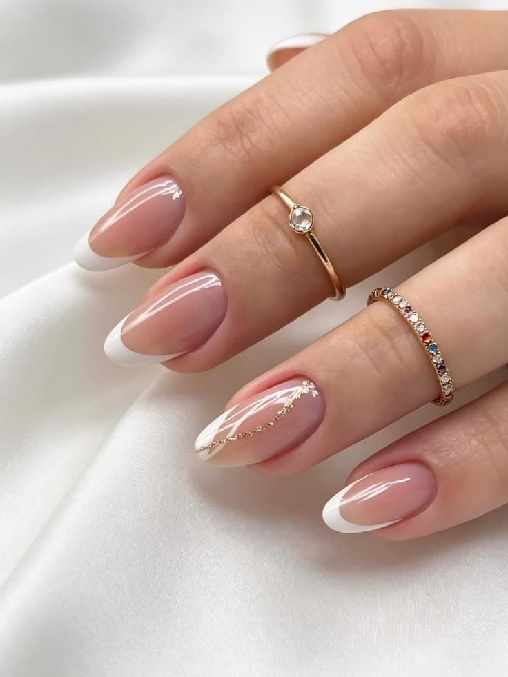 Mão sobre cetim claro com francesinha de pontas brancas e um fio dourado desenhado em uma das unhas.
